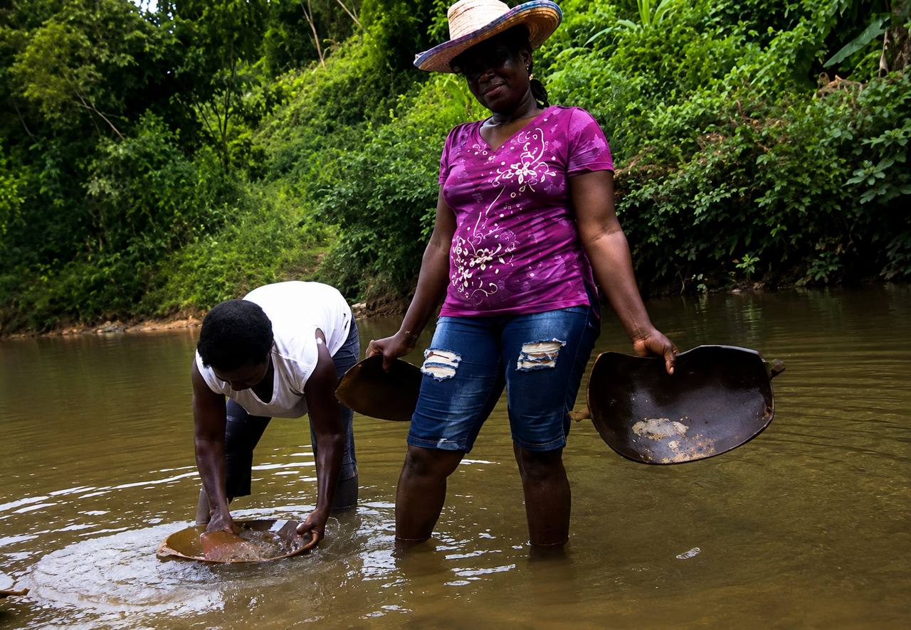 Dos mujeres mineras de subsistencia (barequeras) con bateas en el cauce de un río del Chocó