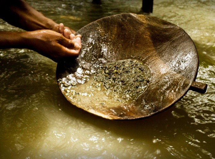 Manos de un minero artesanal lavando oro con batea en el río